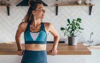 Junge Frau in Sportkleidung steht in der Küche und strahlt Wohlbefinden aus dank Darmgesundheit für Frauen.