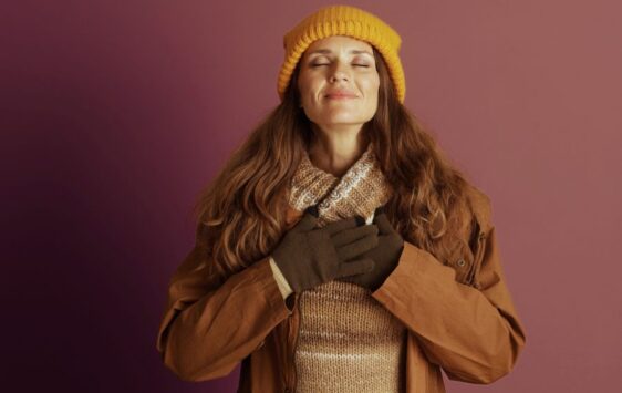 Frau um die 40 hält beide Hände auf ihrem Herzen und strahlt positive Energie dank Selbstfürsorge aus