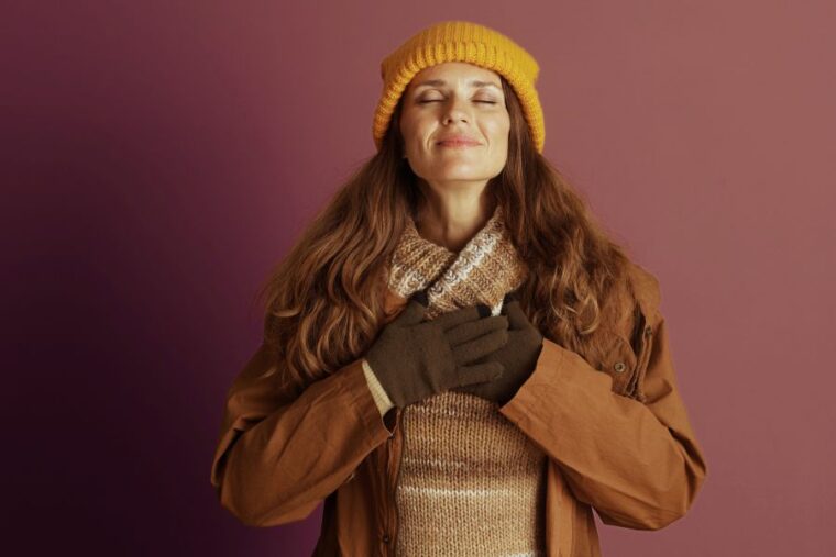 Frau um die 40 hält beide Hände auf ihrem Herzen und strahlt positive Energie dank Selbstfürsorge aus